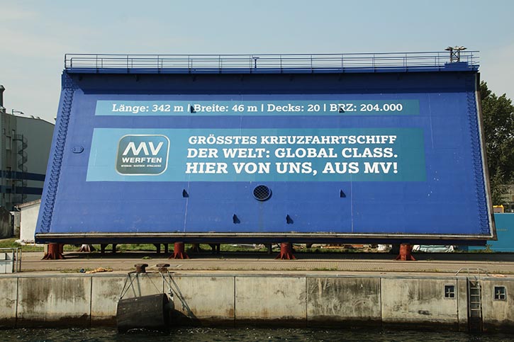 An der Kaikante in Warnemünde wirbt MV Werften auf einem Stahlschild für die „Global Class“